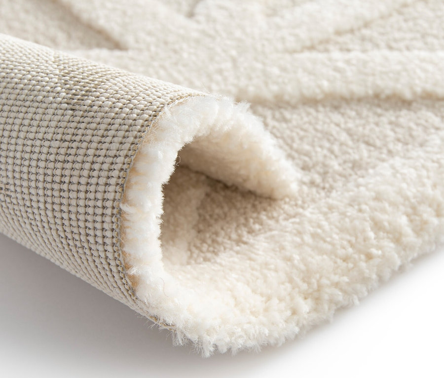 Detailansicht eines cremefarbenen Teppichs »Cosmo« Geo mit geometrischem Muster, teilweise aufgerollt.