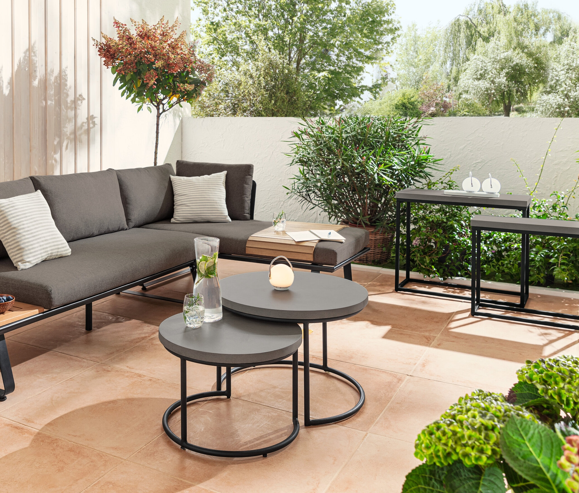 Lounge-Ecke mit modernem Kufengestell, Couchtisch- und Konsolentisch-Set mit Polyzement-Tischplatte und flexibles Teak-Sofatablett auf einer Terrasse.