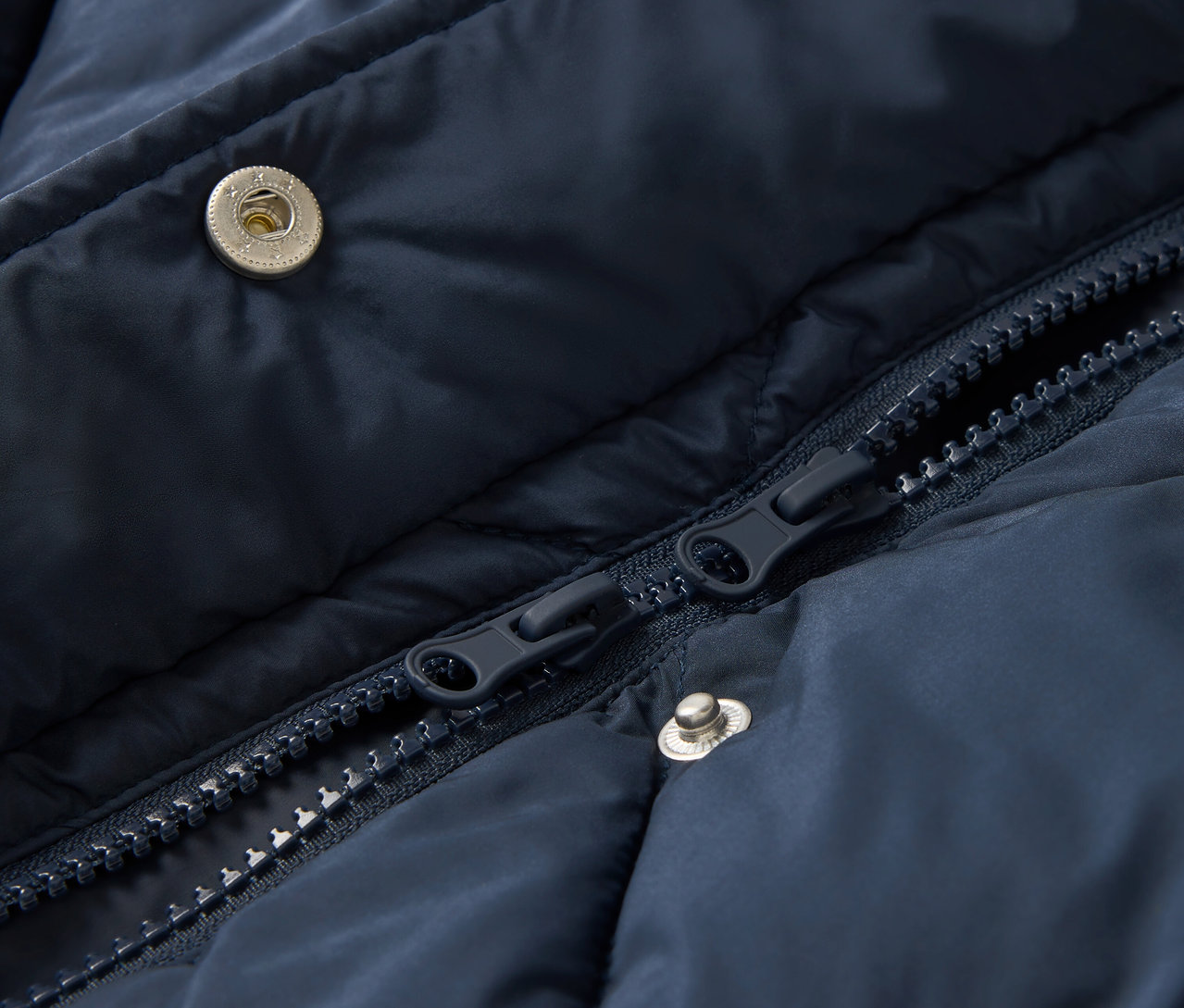 Detailansicht einer marineblauen Steppjacke mit Reißverschluss und Druckknöpfen.
