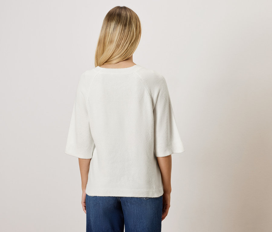 Rückansicht einer Frau mit blonden Haaren in einer weißen Bluse und blauen Jeans.