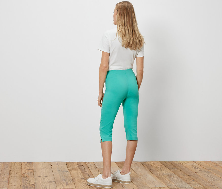 Frau steht mit dem Rücken zur Kamera und trägt eine türkise 3/4-Stretchhose.