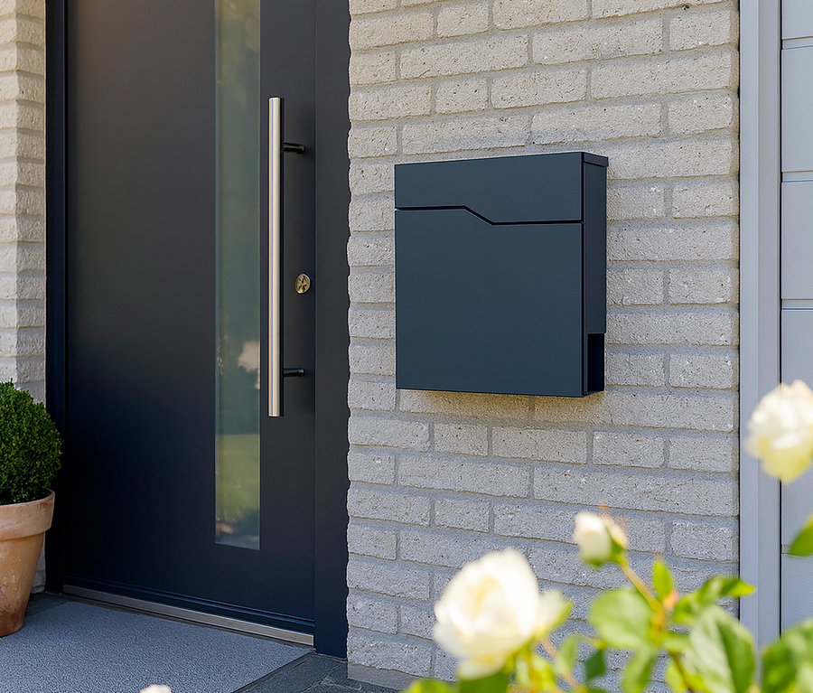 Dunkelblauer rechteckiger Briefkasten an einer hellgrauen Backsteinmauer neben einer dunkelblauen Tür mit silbernem Griff.