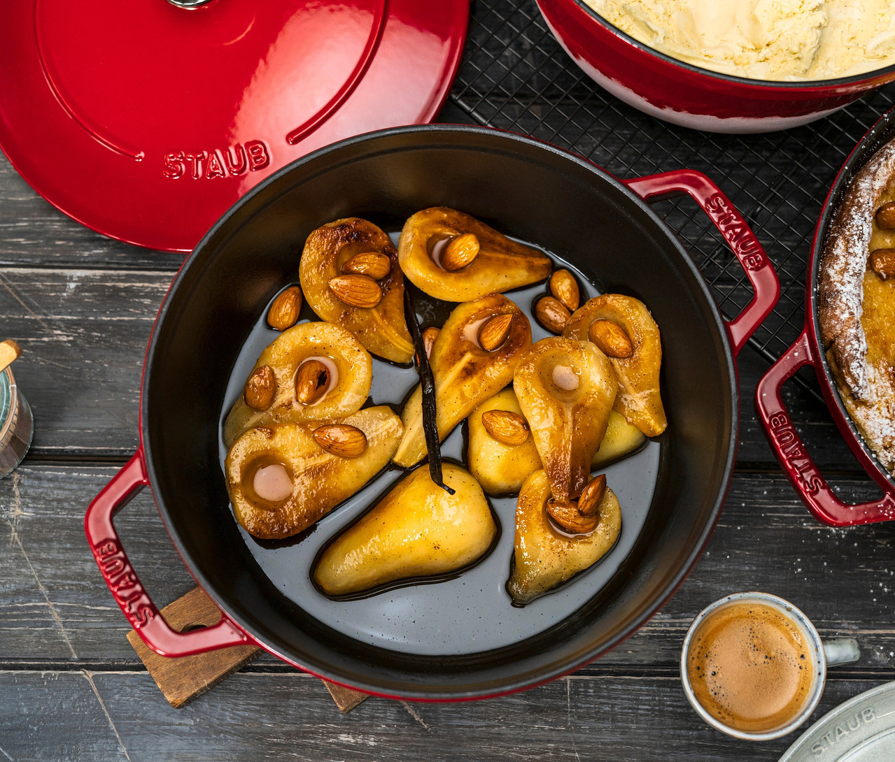 Birnen mit Mandeln in rotem STAUB Kochtopf-Set »La Cocotte«, 3-teilig. Daneben ein Espresso und weitere Speisen.