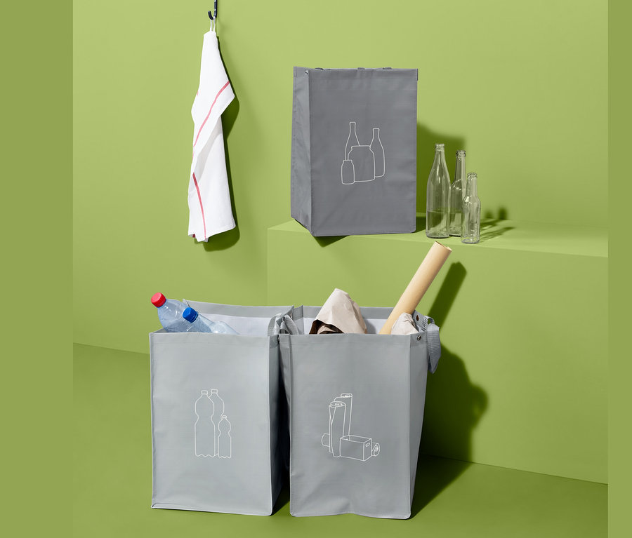 Drei graue Recycling-Abfall-Sortiertaschen mit grafischen Symbolen, eine davon mit PET-Flaschen.