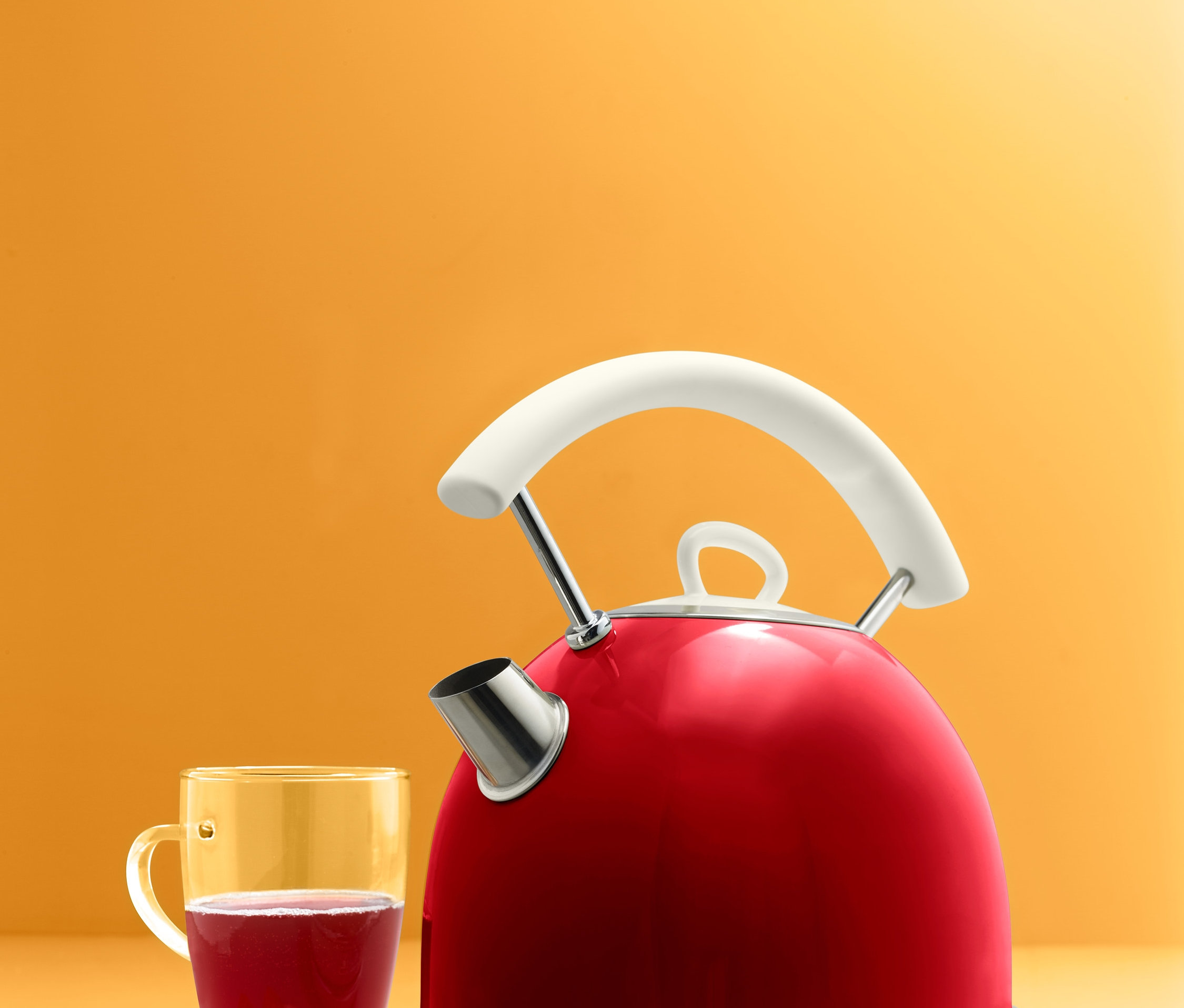 Ein roter Wasserkocher steht neben einem Glas mit Getränk und Keksen.