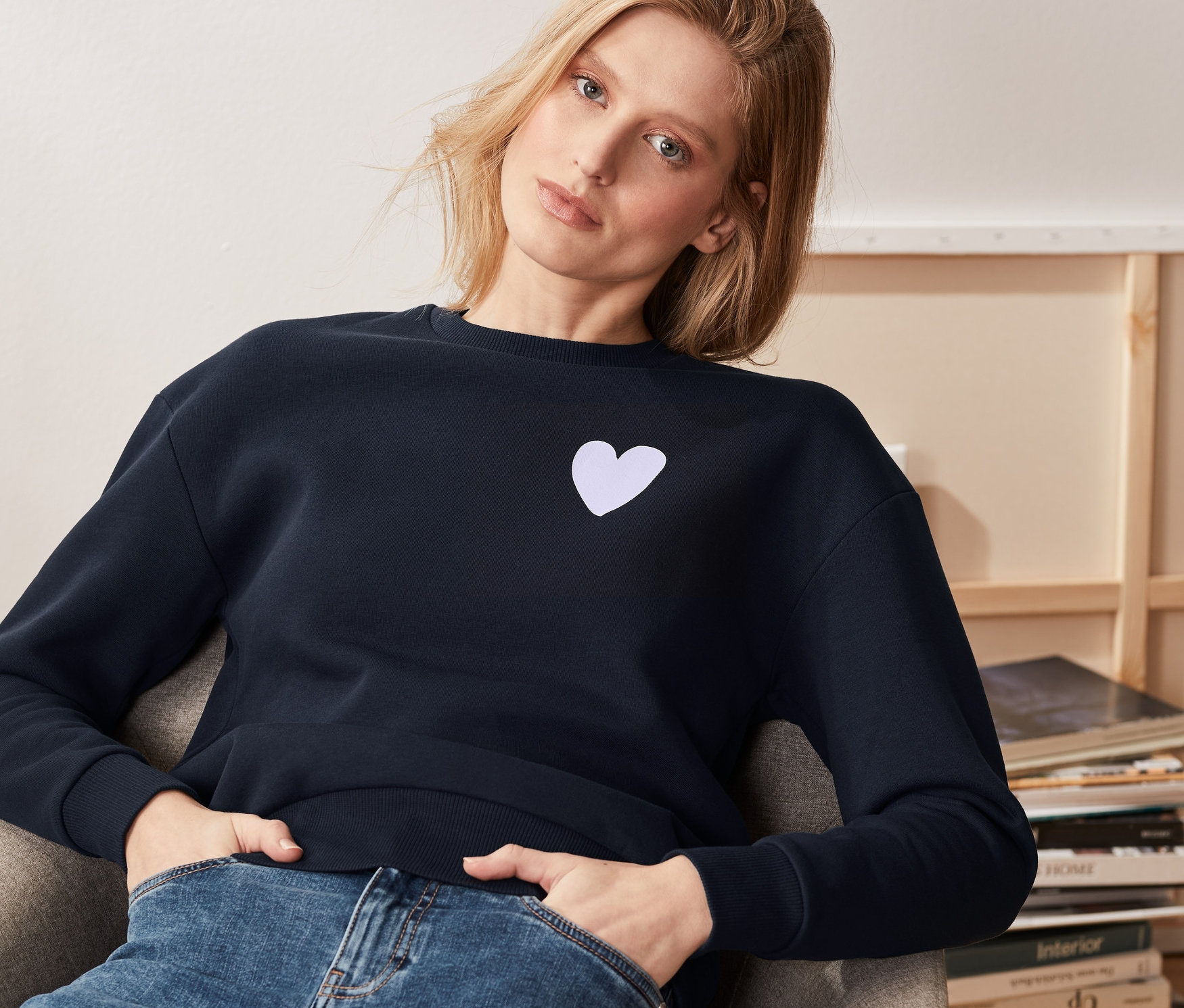 Eine Frau sitzt in einem Sessel und trägt ein dunkelblaues Sweatshirt.