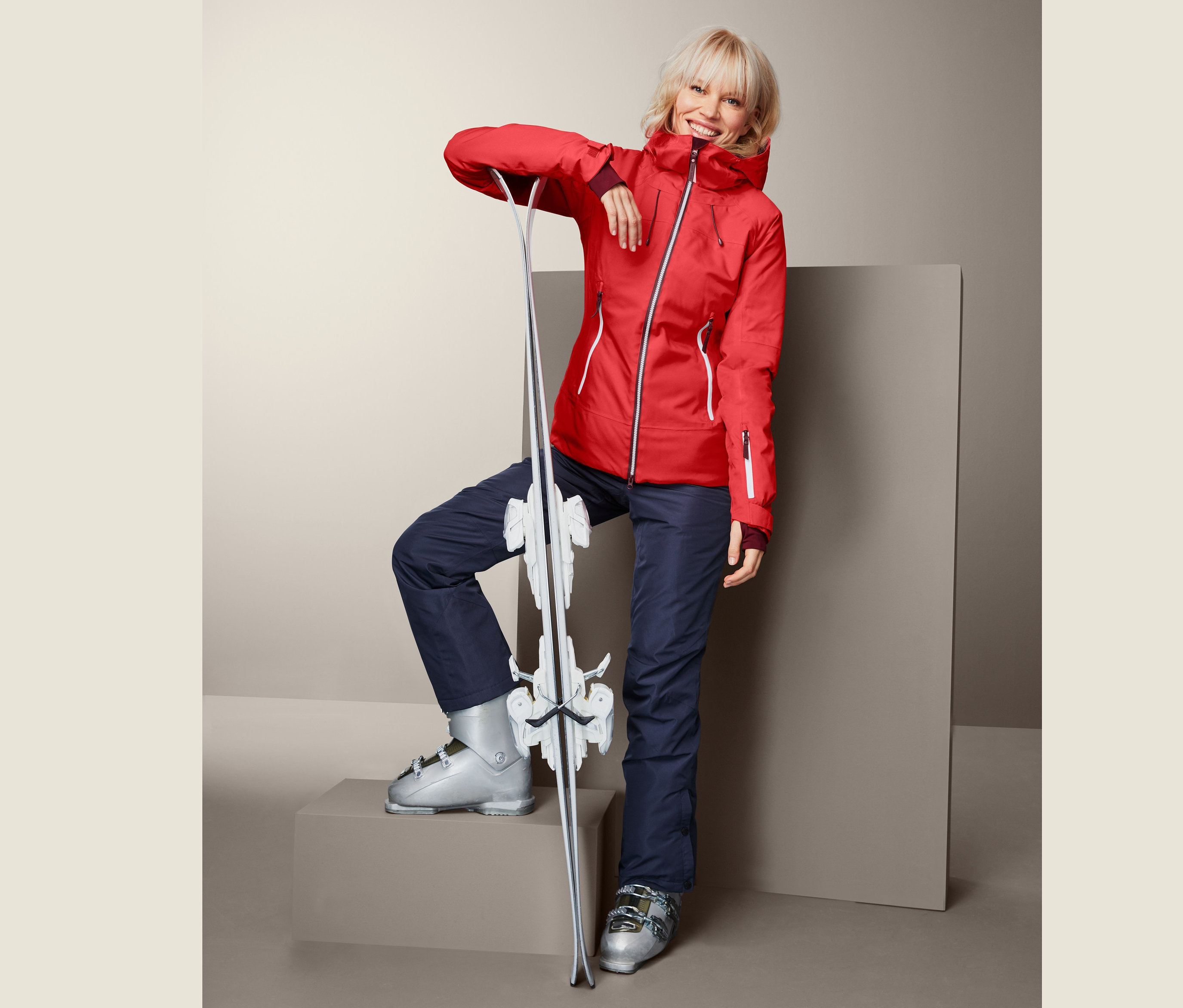 Frau in roter Skijacke, die sich an Ski anlehnt.