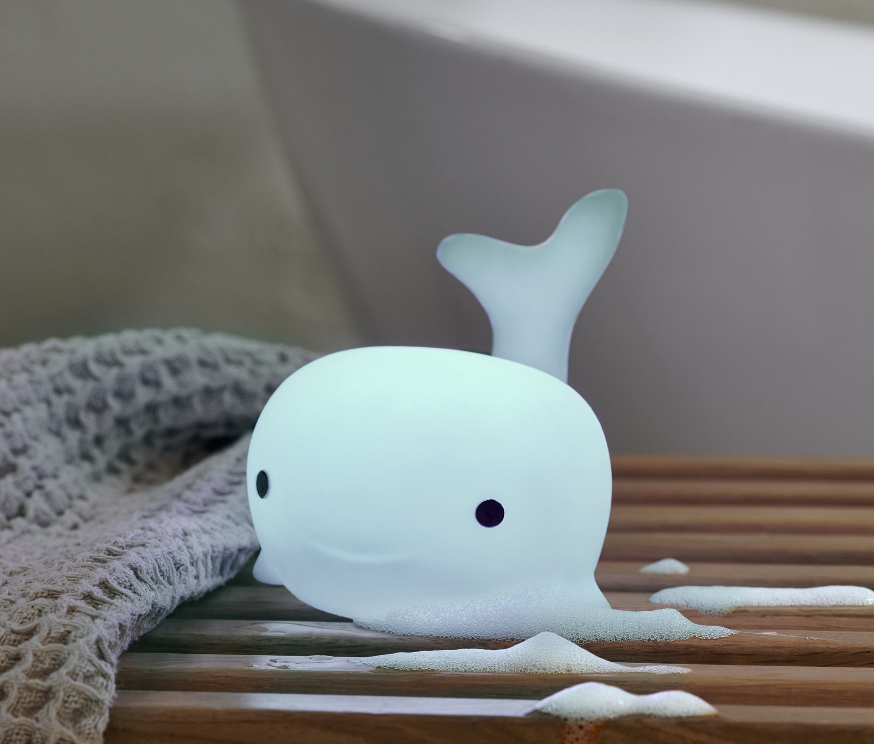 LED-Bade-Wal liegt auf einer Holzablage neben einem grauen Tuch.