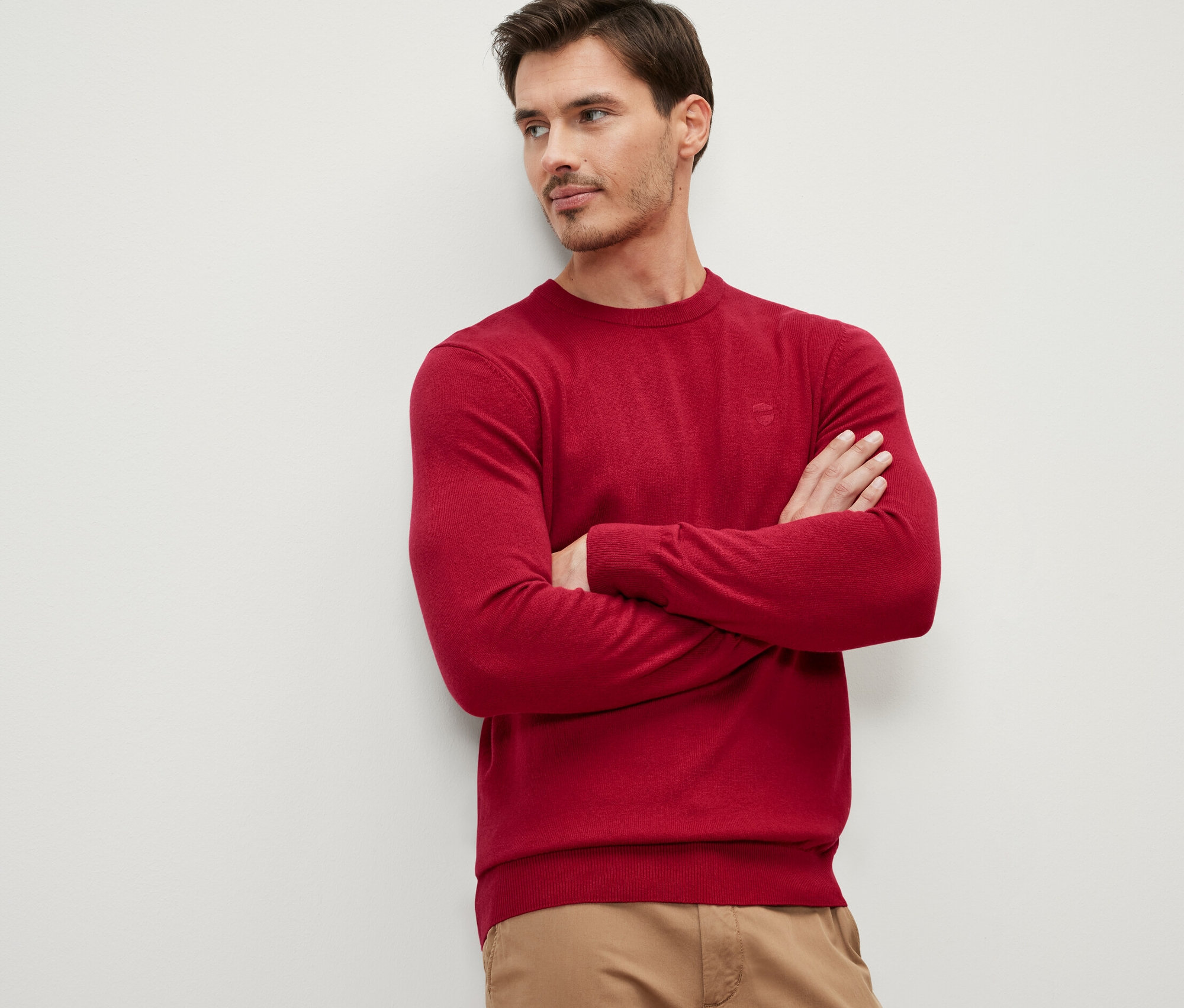 Mann mit verschränkten Armen trägt einen roten Pullover mit Rundhalsausschnitt.