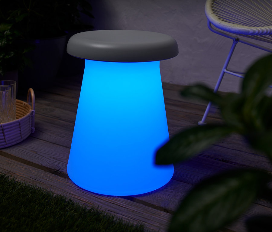Ein blau leuchtender LED-Hocker mit Farbwechsel steht auf einer Holzterrasse.