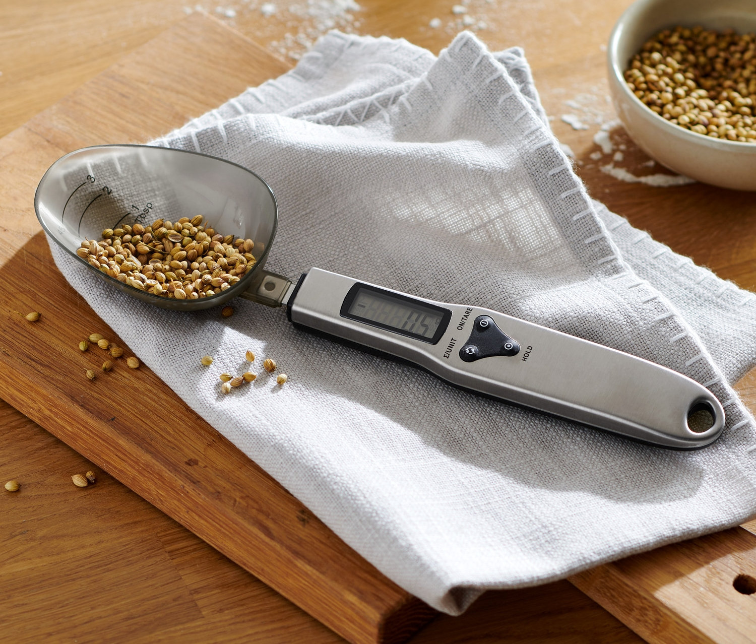 Digitale Löffelwaage mit Gewürzen liegt auf einem Brettchen mit einer Schüssel Teig.