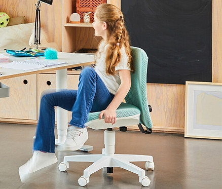 Mädchen sitzt auf einem mintfarbenen Topstar Sitness »Home S'cool« Stuhl an einem weißen Tisch.