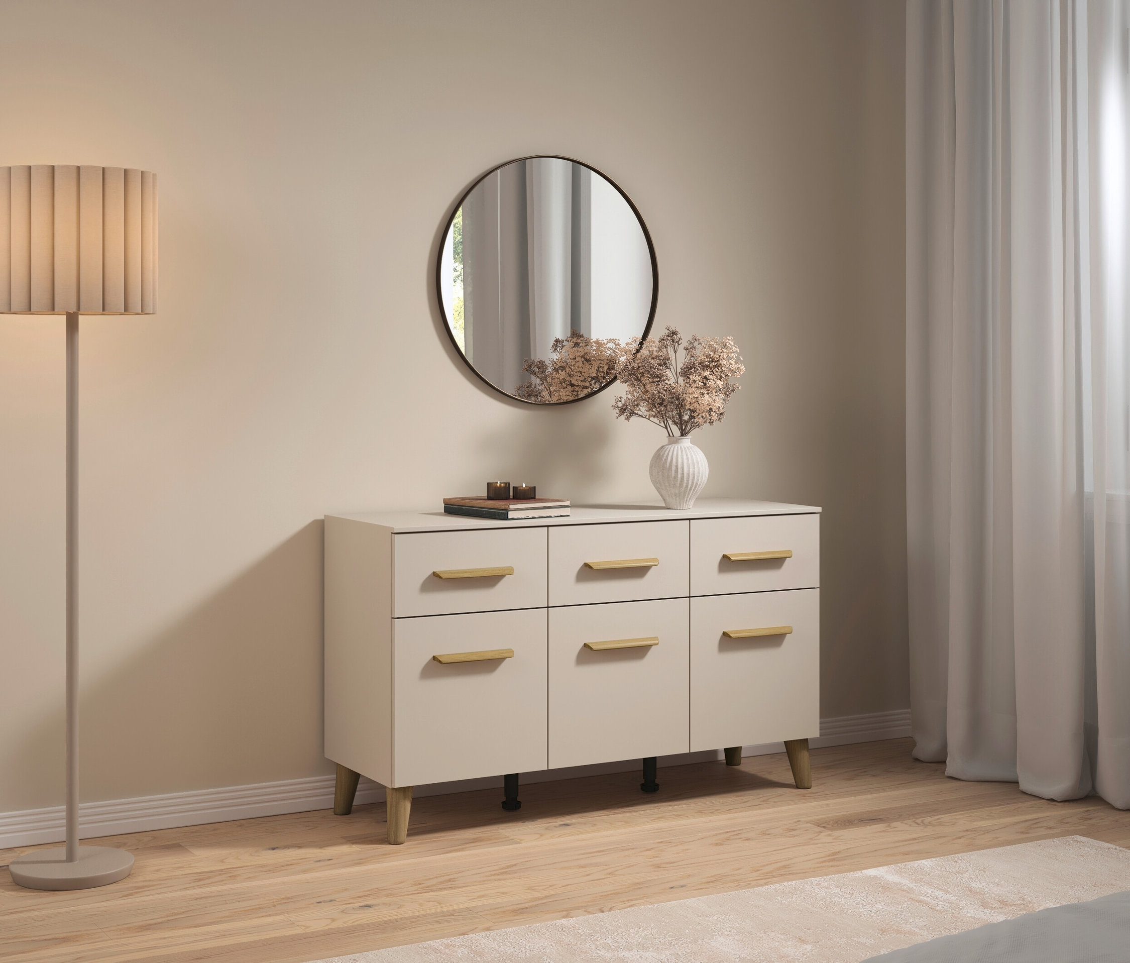 Im Wohnzimmer steht eine Kommode mit sechs Schubladen, über der ein runder Spiegel hängt. Im Zimmer befinden sich auch eine Stehlampe und eine Blumenvase.