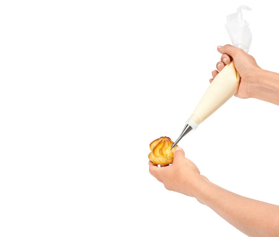 Eine Hand füllt ein Gebäckstück mit Creme aus einem Spritzbeutel.