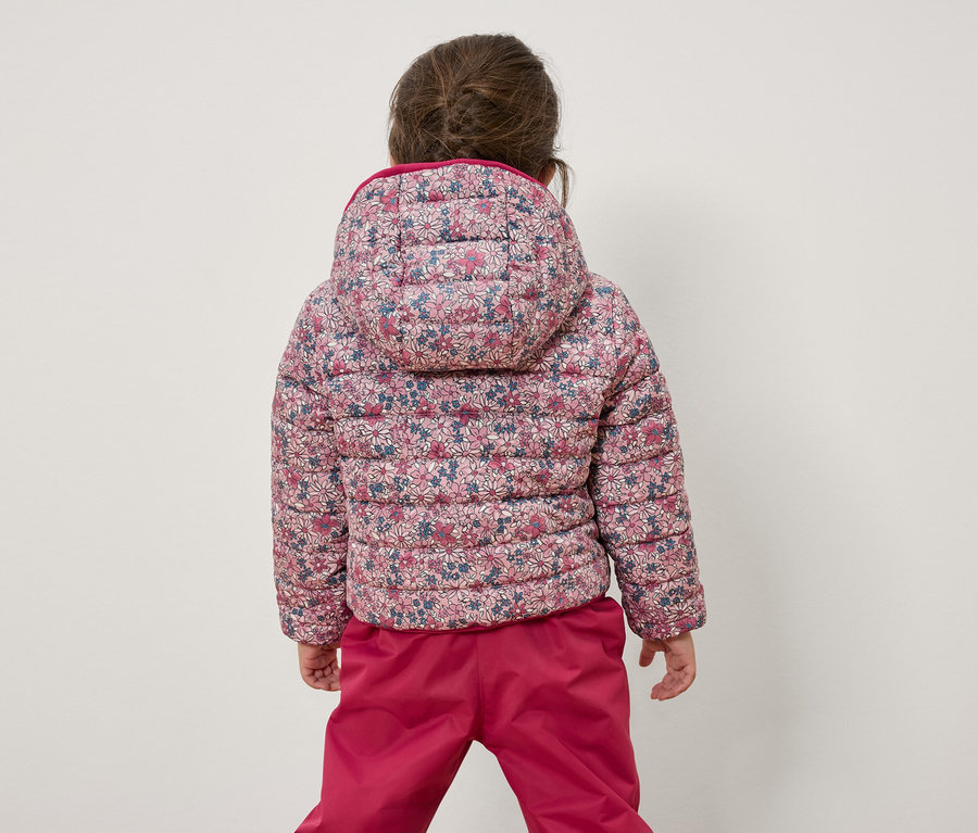 Mädchen mit dem Rücken zur Kamera trägt eine geblümte Jacke und eine pinke Hose.