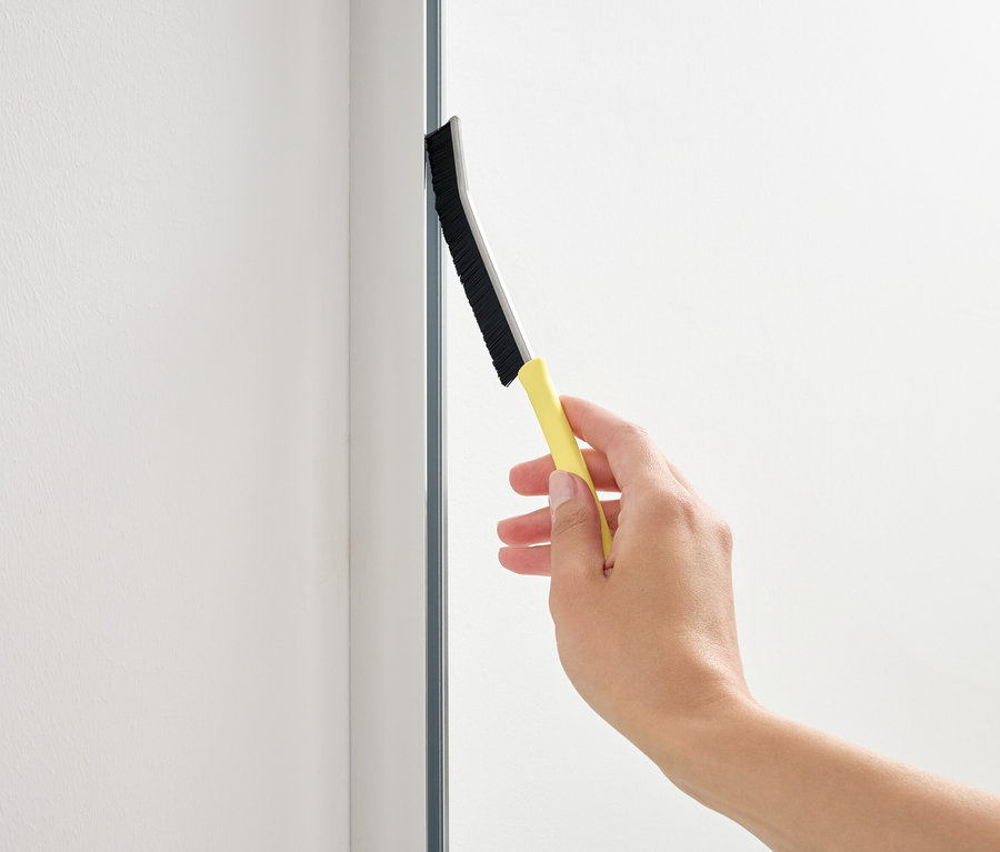 Eine Hand benutzt einen Abzieher mit gelbem Griff auf einer Glasfläche.