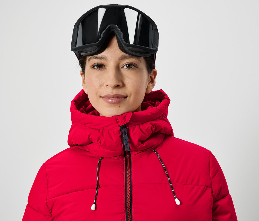 Porträt einer Frau mit Skibrille auf dem Kopf und einer roten Jacke.
