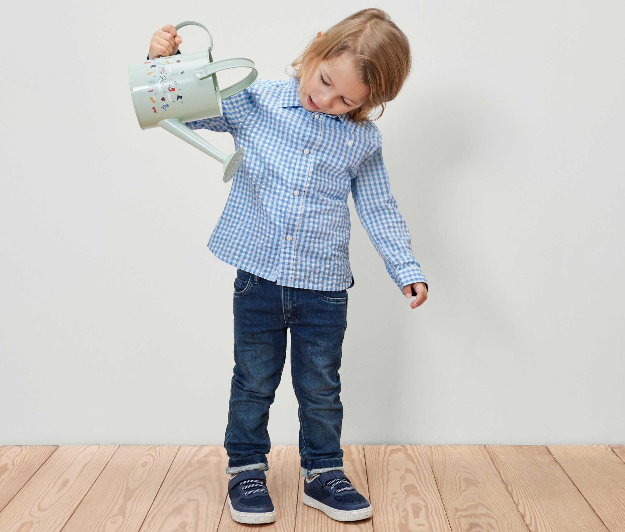 Junge hält hellblaue Gießkanne in der Hand. Er trägt ein Kinderhemd.