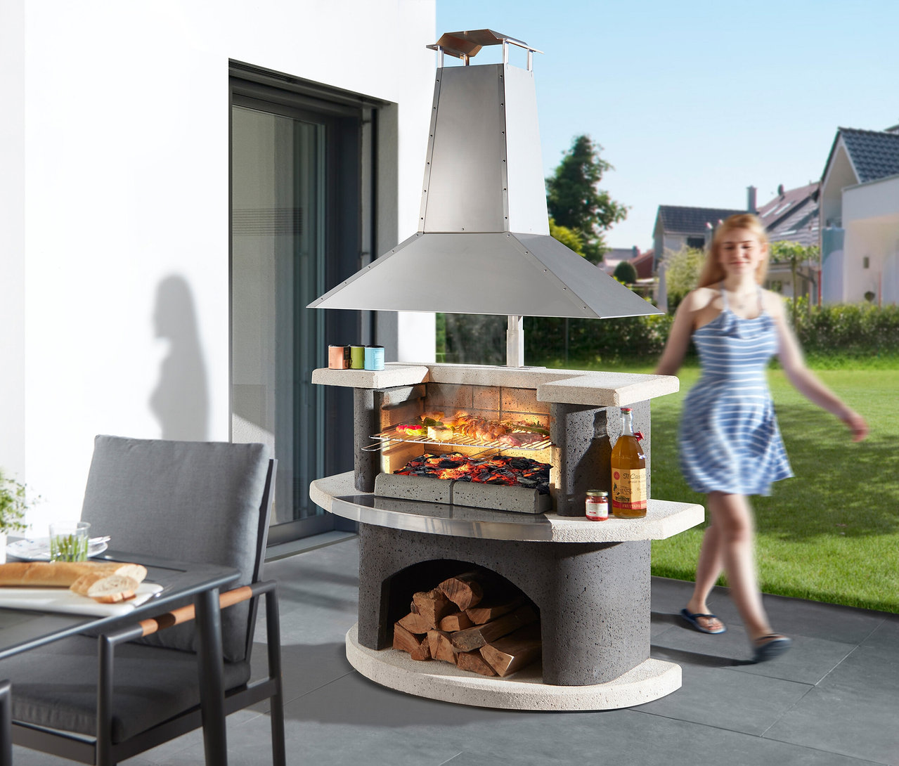 Draußen steht ein gemauerter Grill mit einer Frau im Hintergrund, die vorbeigeht.