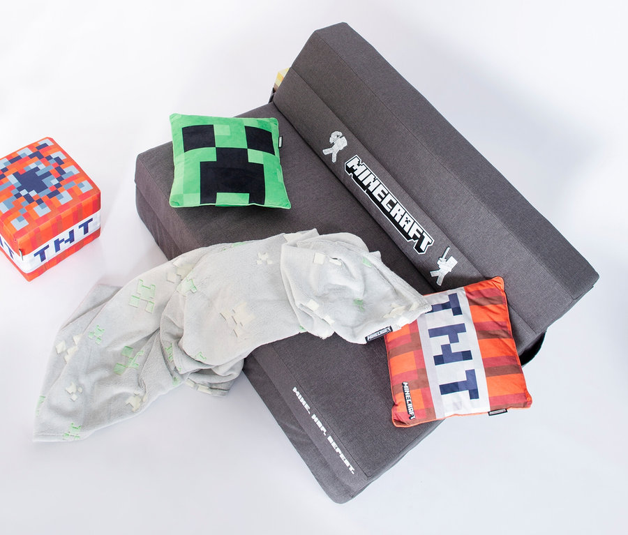 Ein graues Roba Minecraft Gaming Sofa ist auf einem weißen Hintergrund drapiert, zusammen mit einem TNT-Würfel, einem Creeper-Kissen, einem TNT-Kissen und einer grauen Decke.