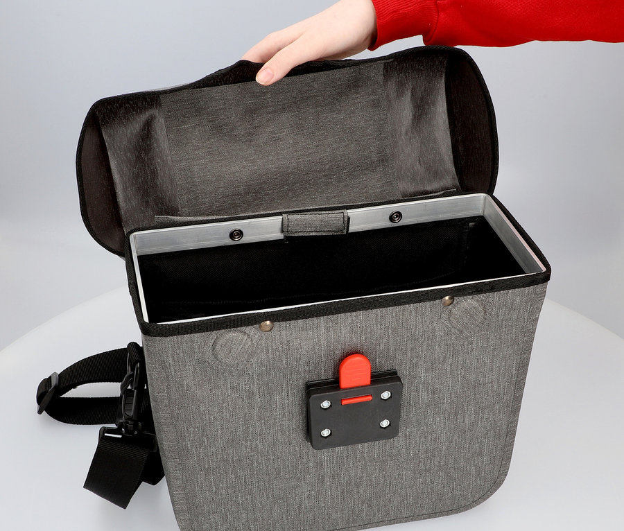 Hand öffnet graue Fahrradtasche mit schwarzem Verschluss und schwarzem Gurt.