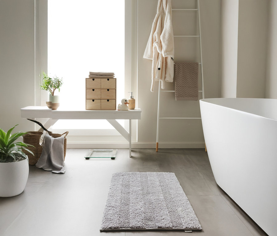 Eine hellgraue benuta Badematte »Ilka«, 50 x 80 cm liegt auf einem grauen Badezimmerboden.