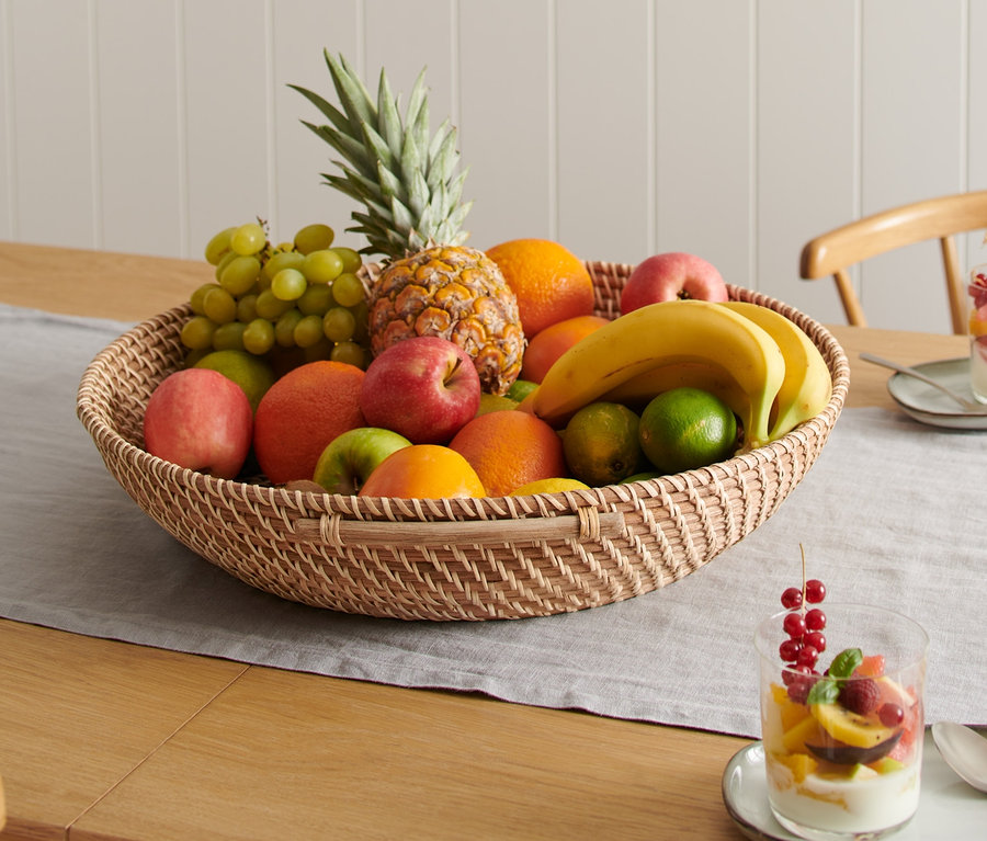 Ein XXL-Rattan-Obstkorb gefüllt mit verschiedenen Früchten steht auf einem Tisch.