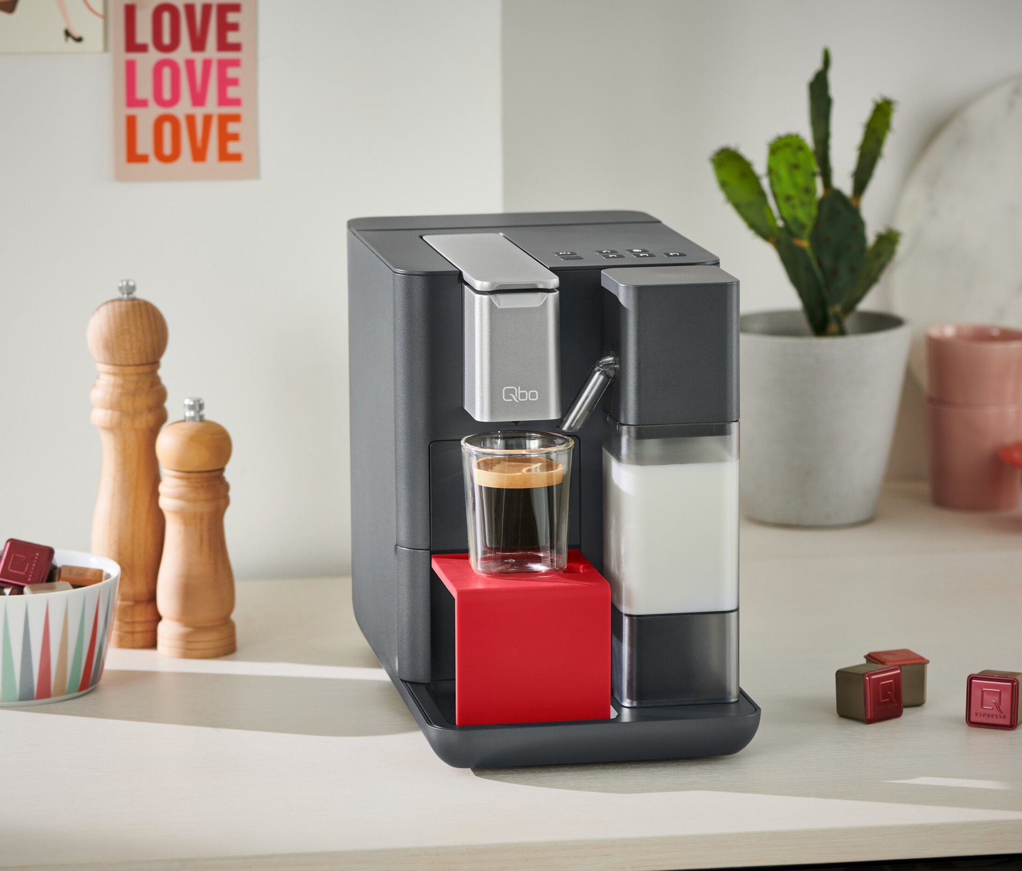 Graue Qbo MILK MASTER Lipstick Red Kaffeemaschine mit einer Tasse Kaffee.