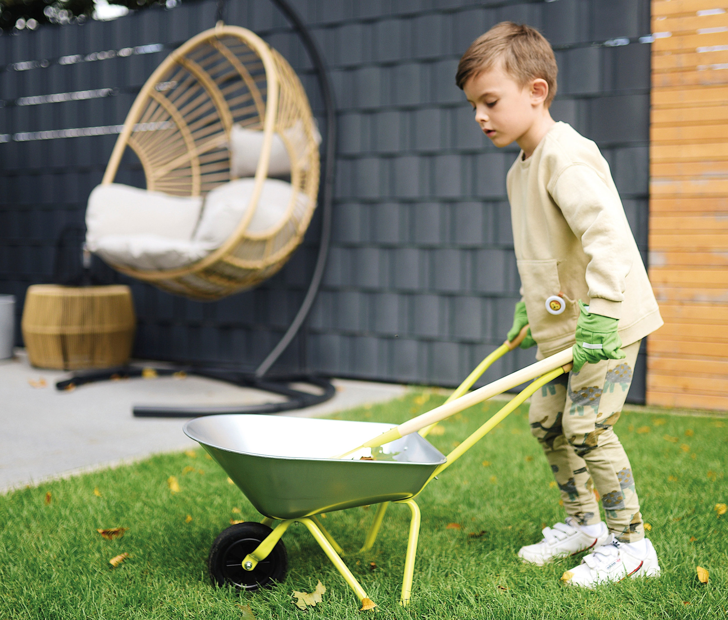 Junge schiebt small foot Schubkarre mit Gartenwerkzeug auf dem Rasen.