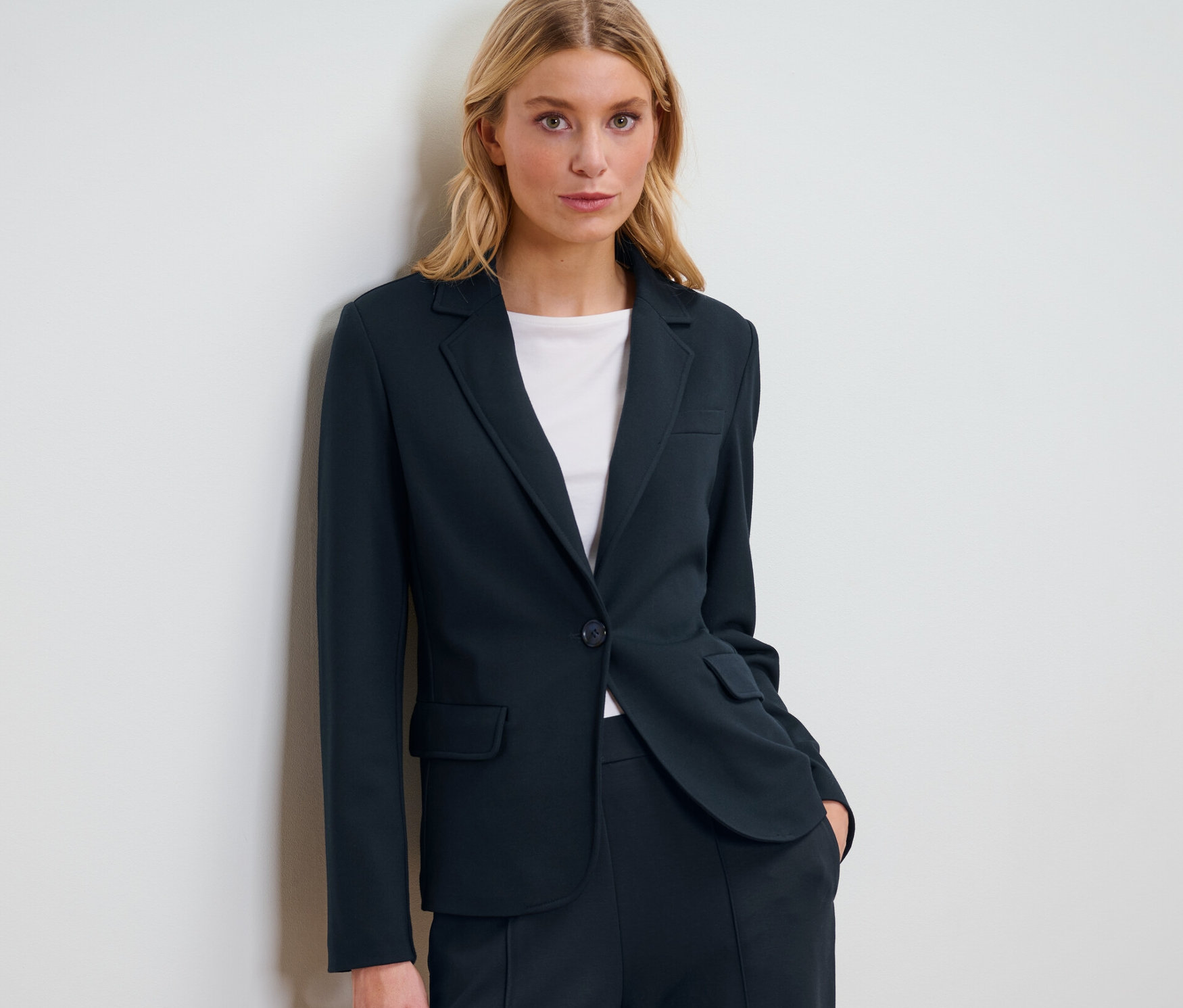 Blonde Frau posiert in einem marineblauen Jerseyblazer.