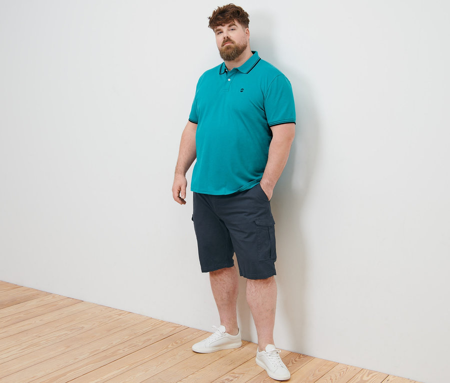 Mann posiert in Piqué-Poloshirt, aqua, und Cargo-Shorts, navy.