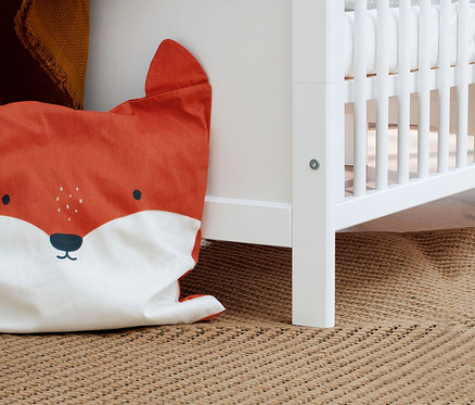 Ein orangefarbenes Kissen in Fuchsform lehnt an einem weißen Pinolino Set »Viktoria« Kinderbett auf einem braunen Teppich.