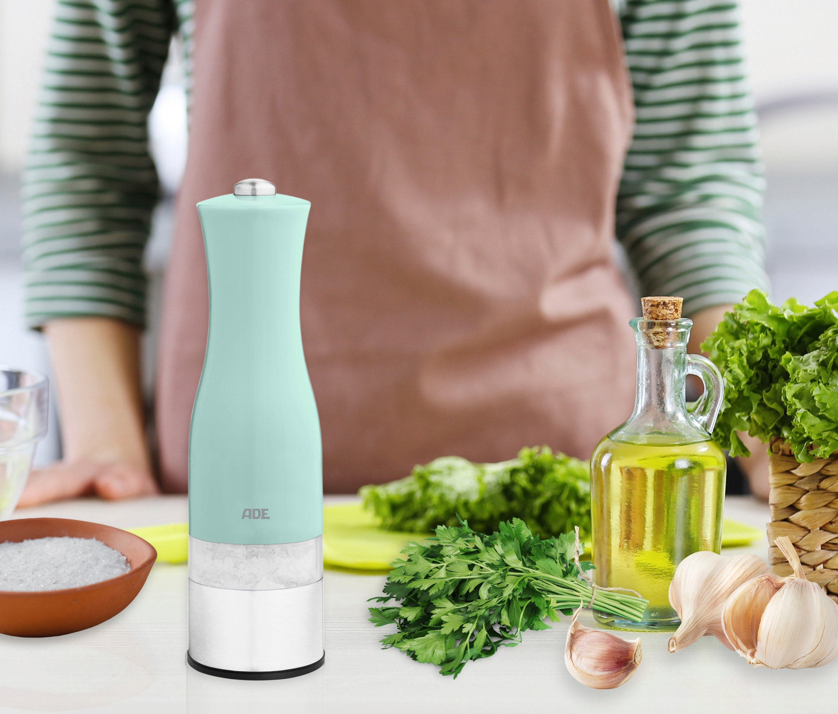 Auf einem Tisch stehen eine ADE Elektrische Salz- und Pfeffermühle mit Beleuchtung, Minze, eine Schale mit Salz, Öl, Knoblauch und Gemüse.