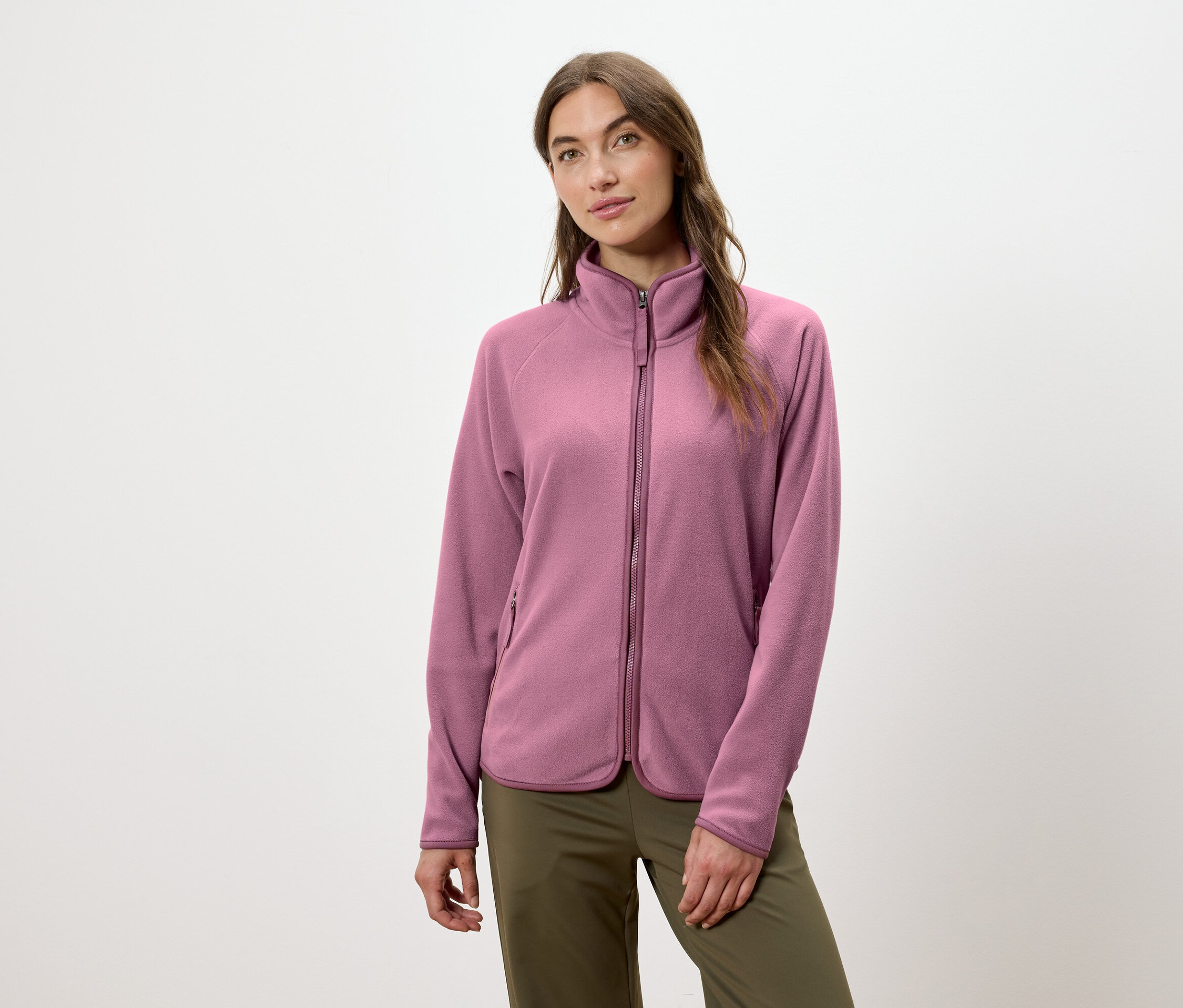 Eine Frau trägt eine rosafarbene Fleecejacke mit Reißverschluss und eine grüne Hose.
