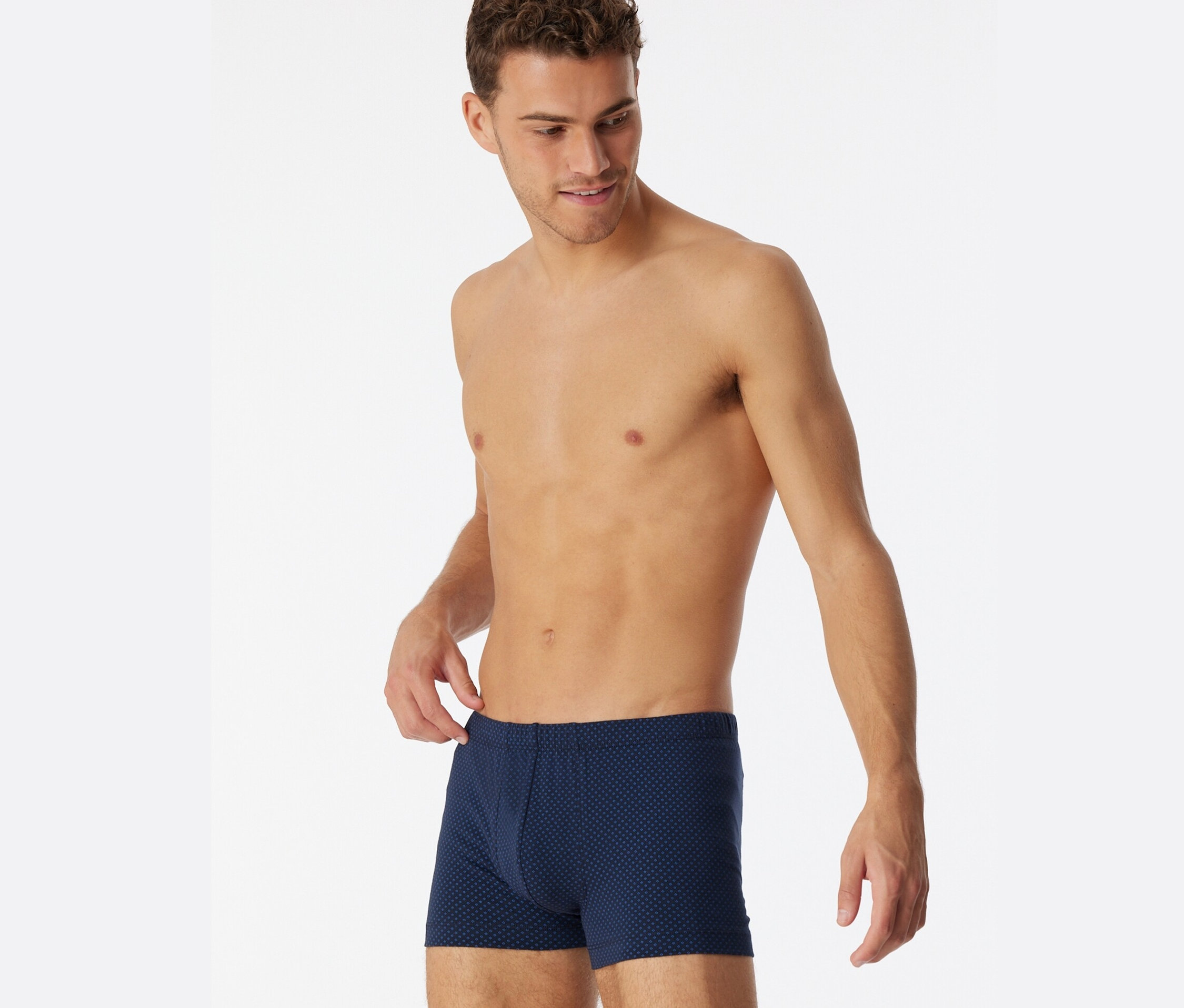 Mann blickt nach unten und hält den Bund der blau gemusterten SCHIESSER Shorts, Alloverprint, fest.