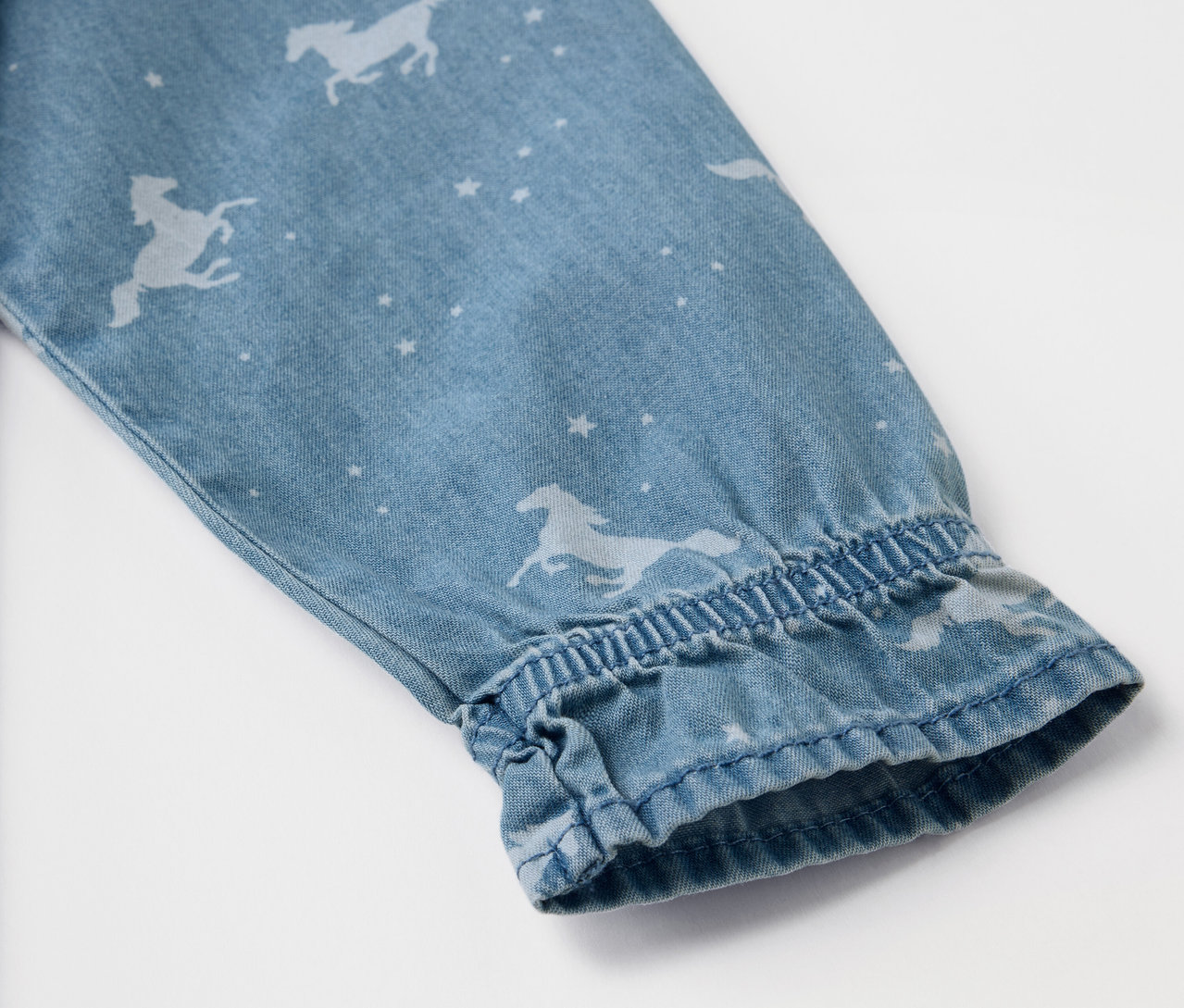 Detail eines Ärmels eines Kinder-Jeanskleids mit Pferde- und Sternenmuster.