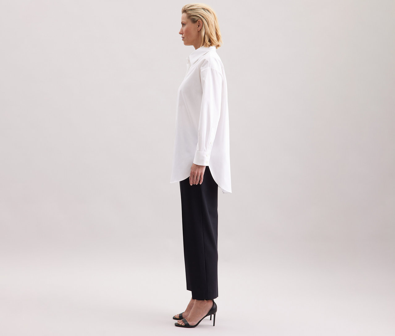 Frau trägt eine weiße Seidensticker Oversize Longbluse, schwarze Hose und hochhackige Schuhe.