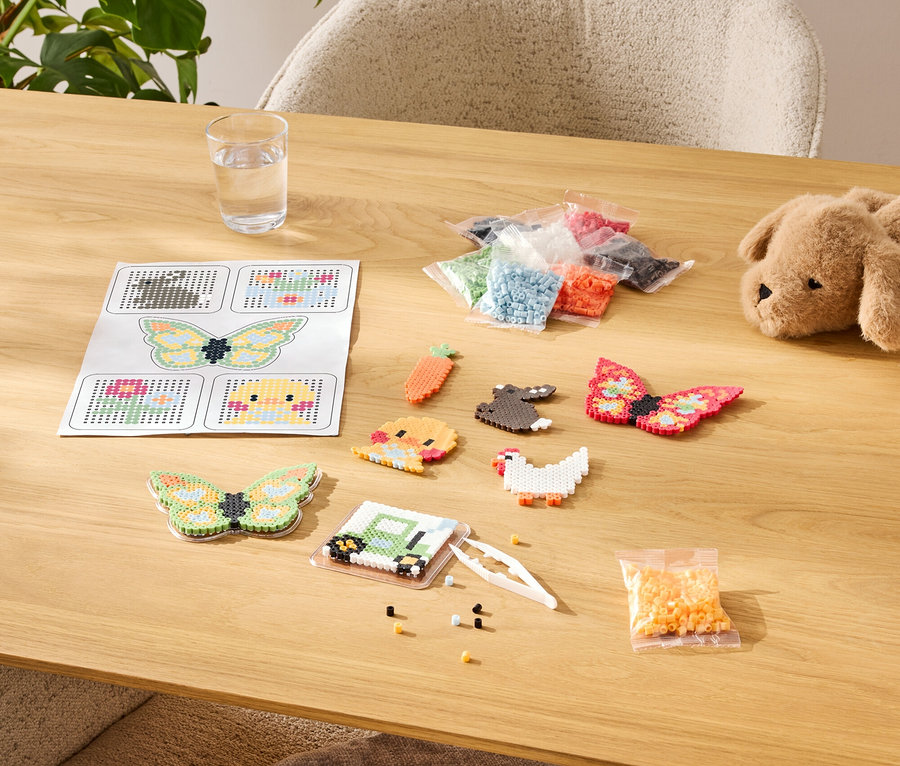 Tisch mit Bügelperlen-Bastelset, darunter Vorlagen, fertige Motive und Farbsortimente in Tüten.