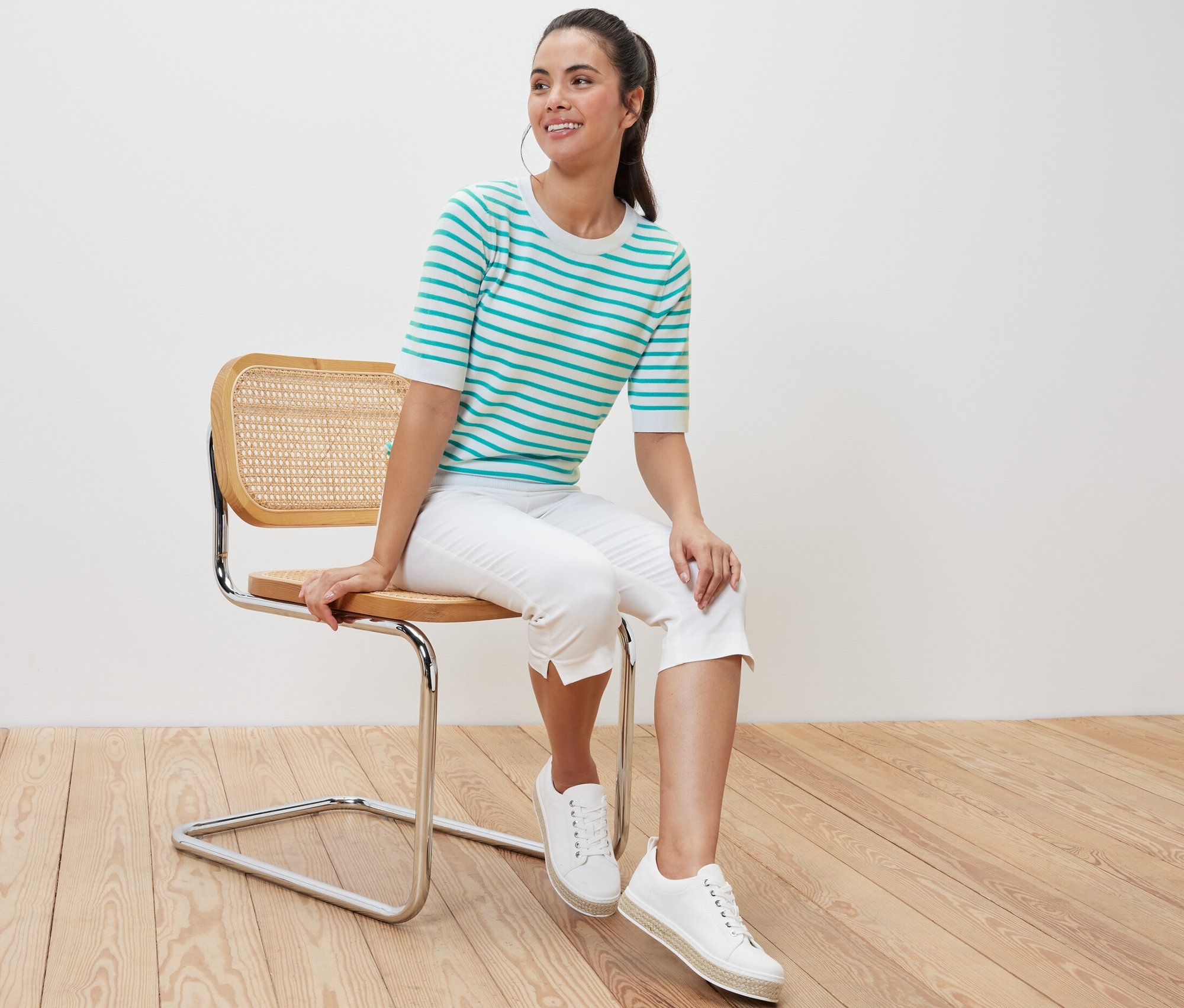 Frau sitzt auf einem Stuhl und trägt einen gestreiften Feinstrickpullover in Aqua.