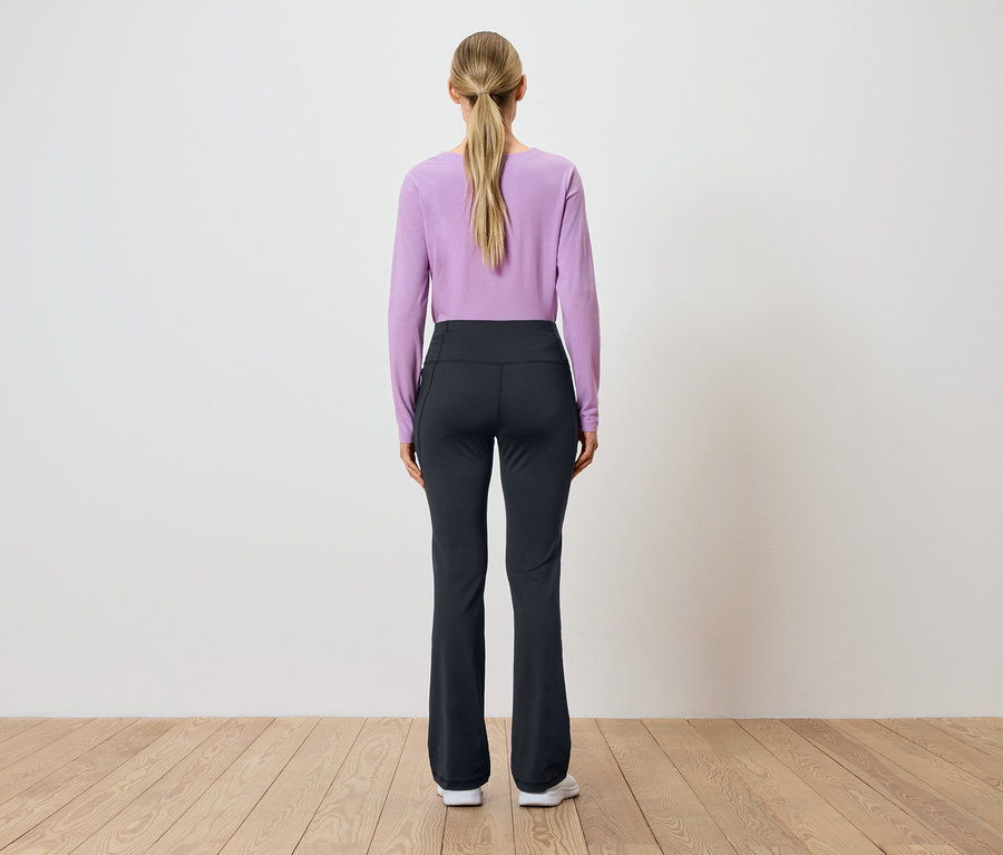 Rückansicht einer Frau mit blonden, zum Pferdeschwanz gebundenen Haaren, die ein lila langärmliges Oberteil und eine schwarze Hose trägt.