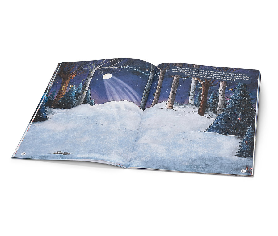 Ein aufgeschlagenes Buch zeigt eine verschneite Waldszene mit einer beleuchteten Lichtung in der Nacht.