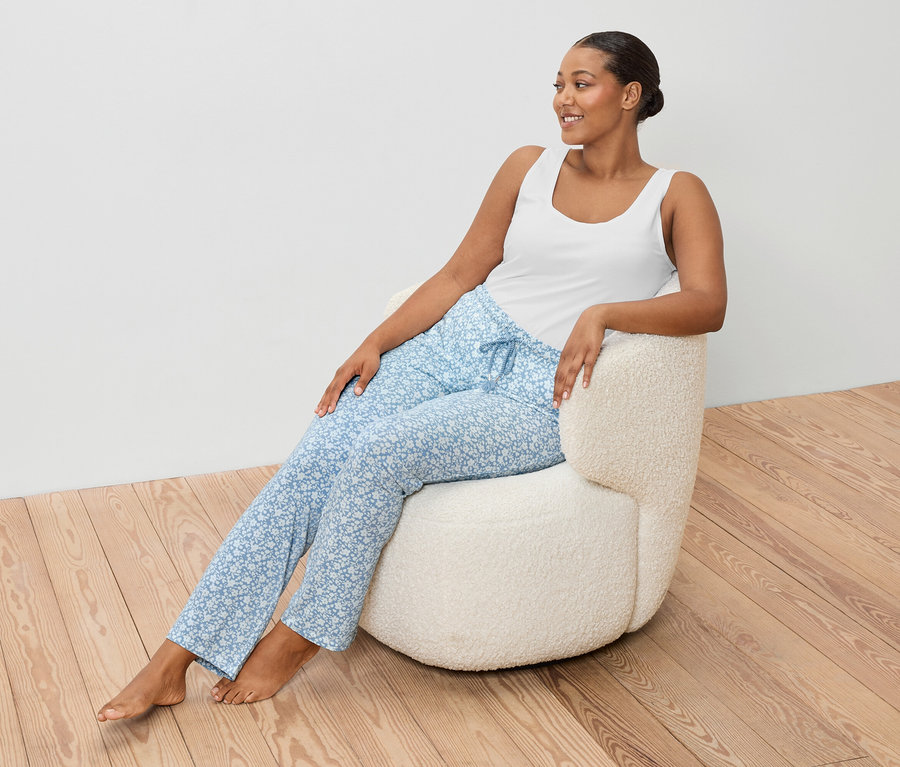 Frau sitzt in einem Sessel und trägt ein weißes Hemdchen und eine blaue Hose.