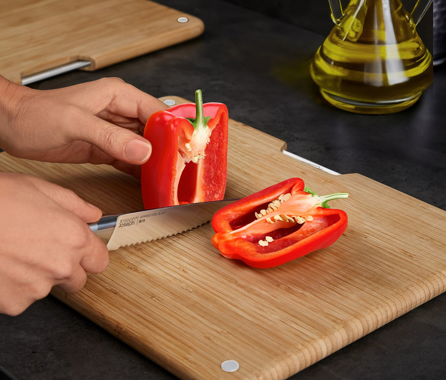 Eine Person schneidet eine rote Paprika auf einem Bambus-Schneidebrett mit einem Messer.