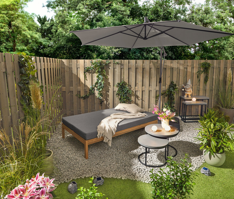 Eine 2-in-1-Gartenbank, die als Doppel-Sonnenliege dient, steht neben zwei Garten-Couchtischen mit Polyzement-Tischplatte (ca. 50 cm und 60 cm Durchmesser). Ein Gartenzwerg mit LED-Laterne steht auf einem der 2 Garten-Konsolentische mit Polyzement-Tischplatten. Drei Akku-Tischleuchten und drei Solar-LED-Steine sind ebenfalls sichtbar.