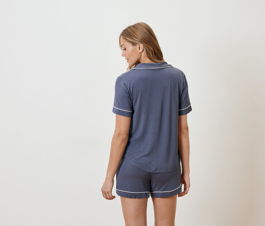 Frau von hinten in marineblauem Kurzarm-Pyjama mit weißer Paspelierung.