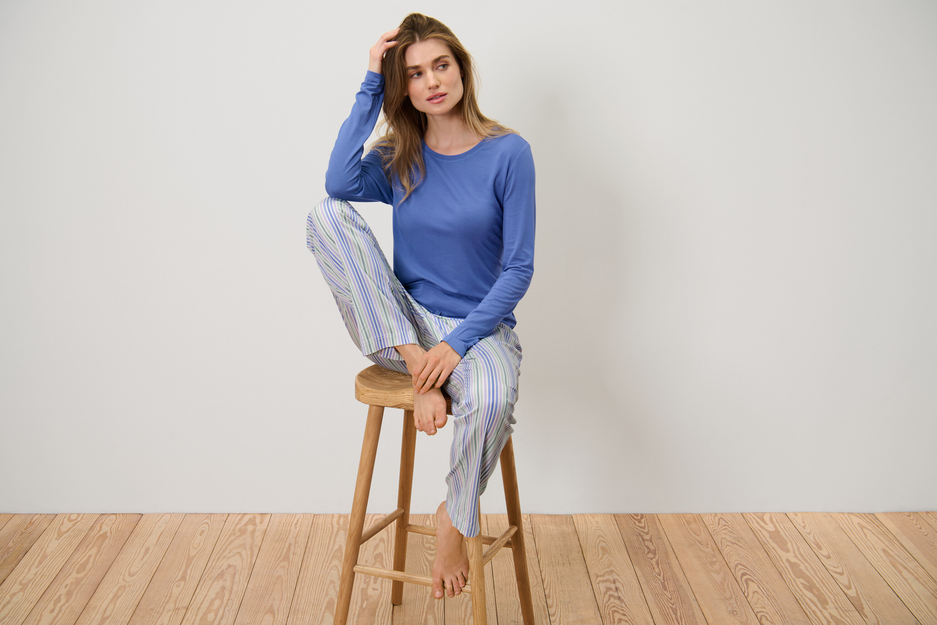 Frau sitzt in einem Pyjama mit Webhose auf einem Hocker.