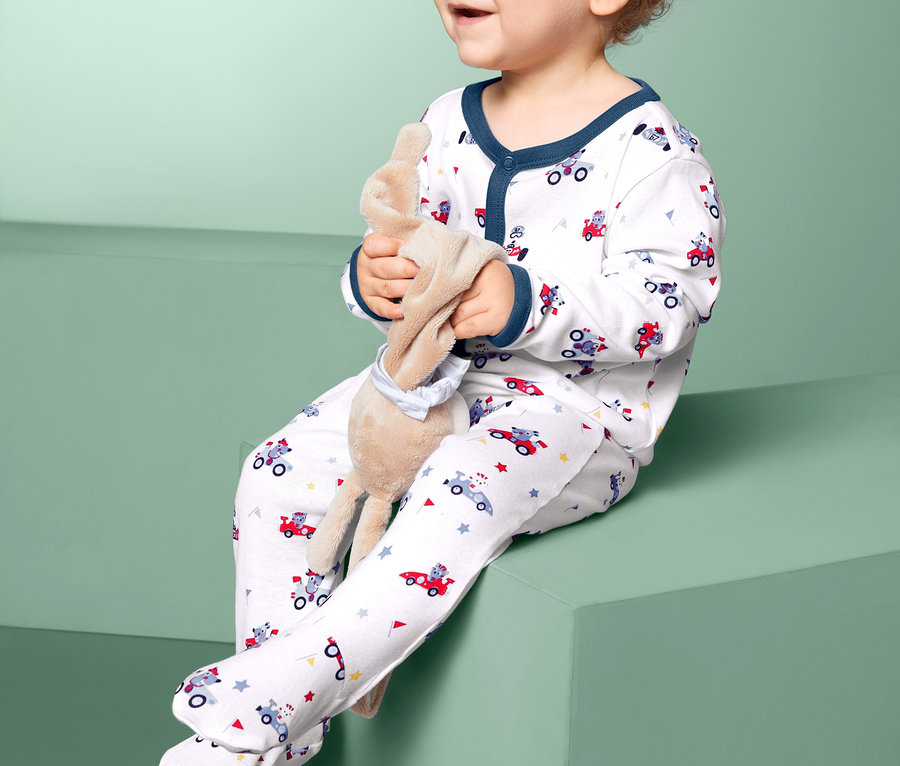 Ein Kind sitzt mit einem Stofftier und trägt 2 Schlafanzüge.