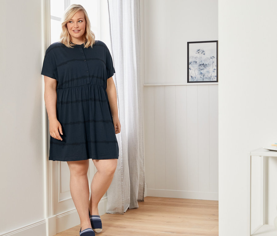 Frau steht an einer Wand und trägt ein Jerseykleid und Espadrilles.