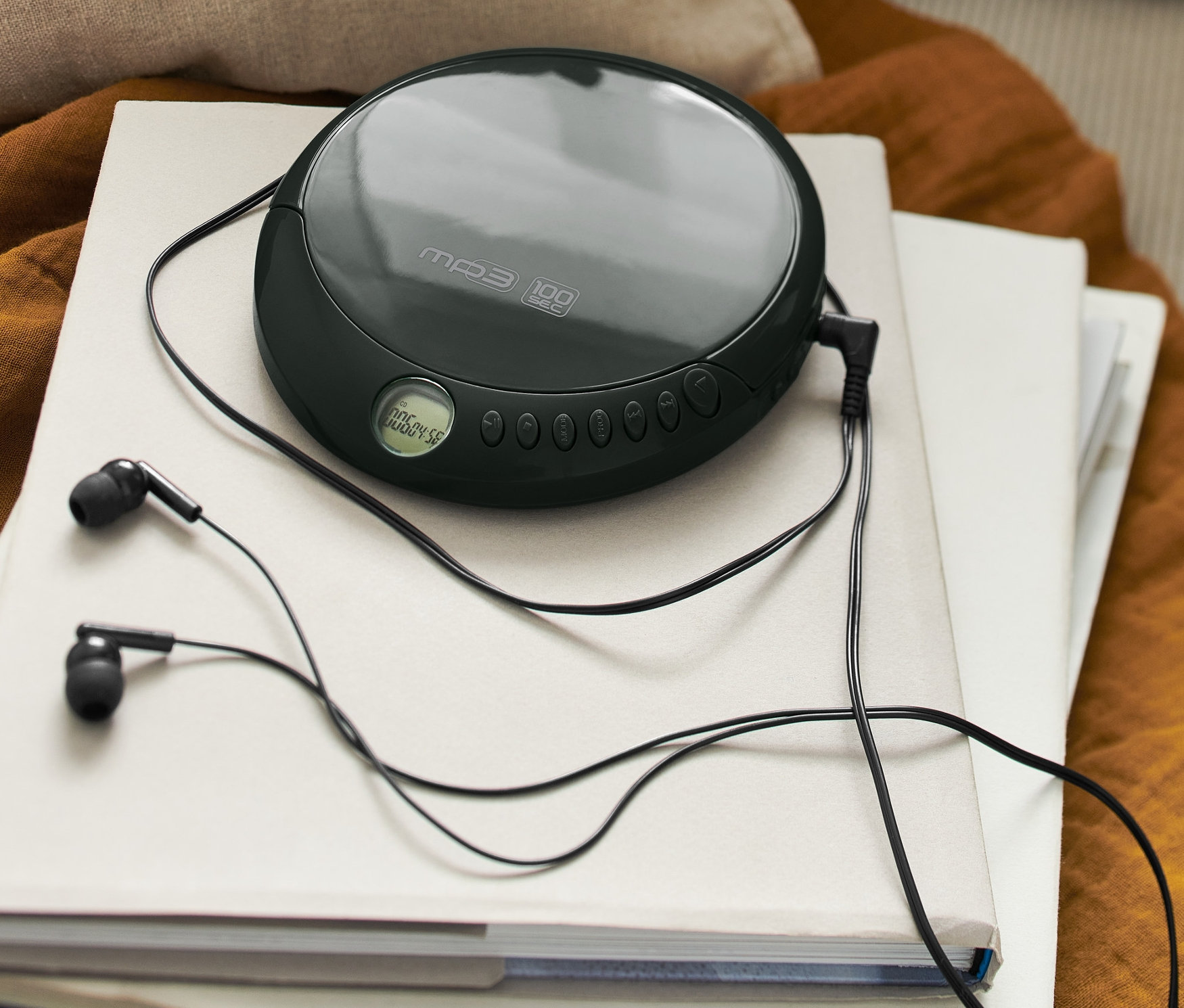 Ein schwarzer, tragbarer CD-Player mit schwarzen Kopfhörern liegt auf einem Stapel Bücher.