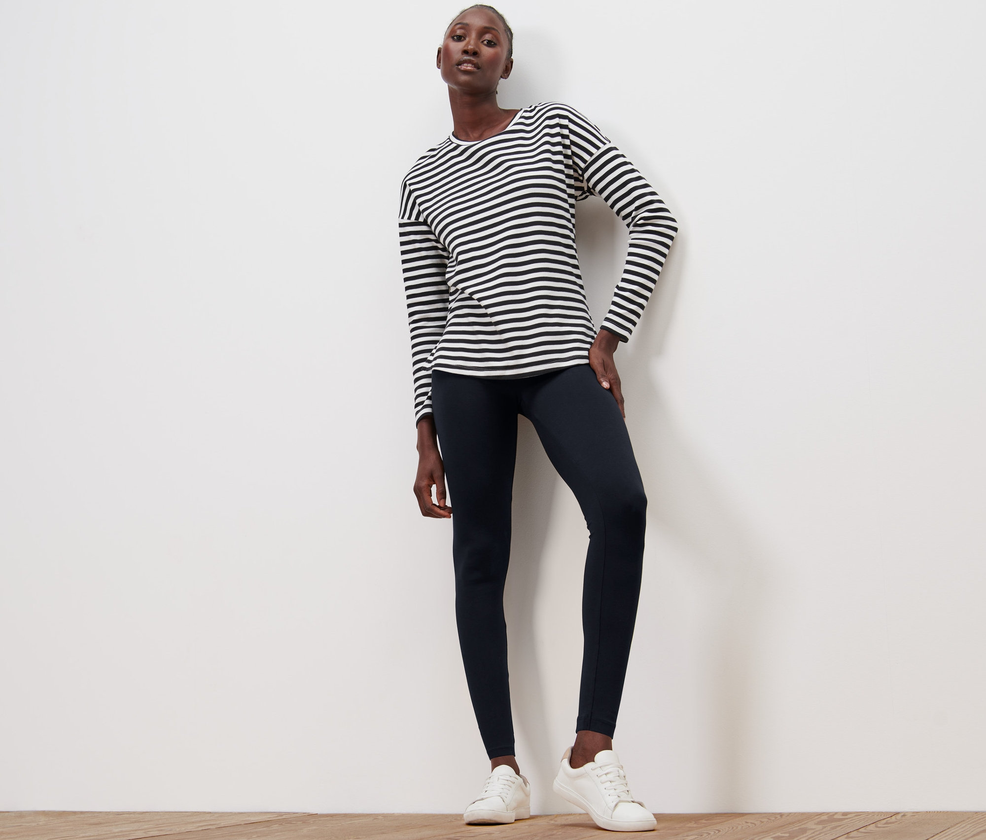 Frau posiert auf Holzboden in schwarzen Leggings und einem gestreiften Oberteil.